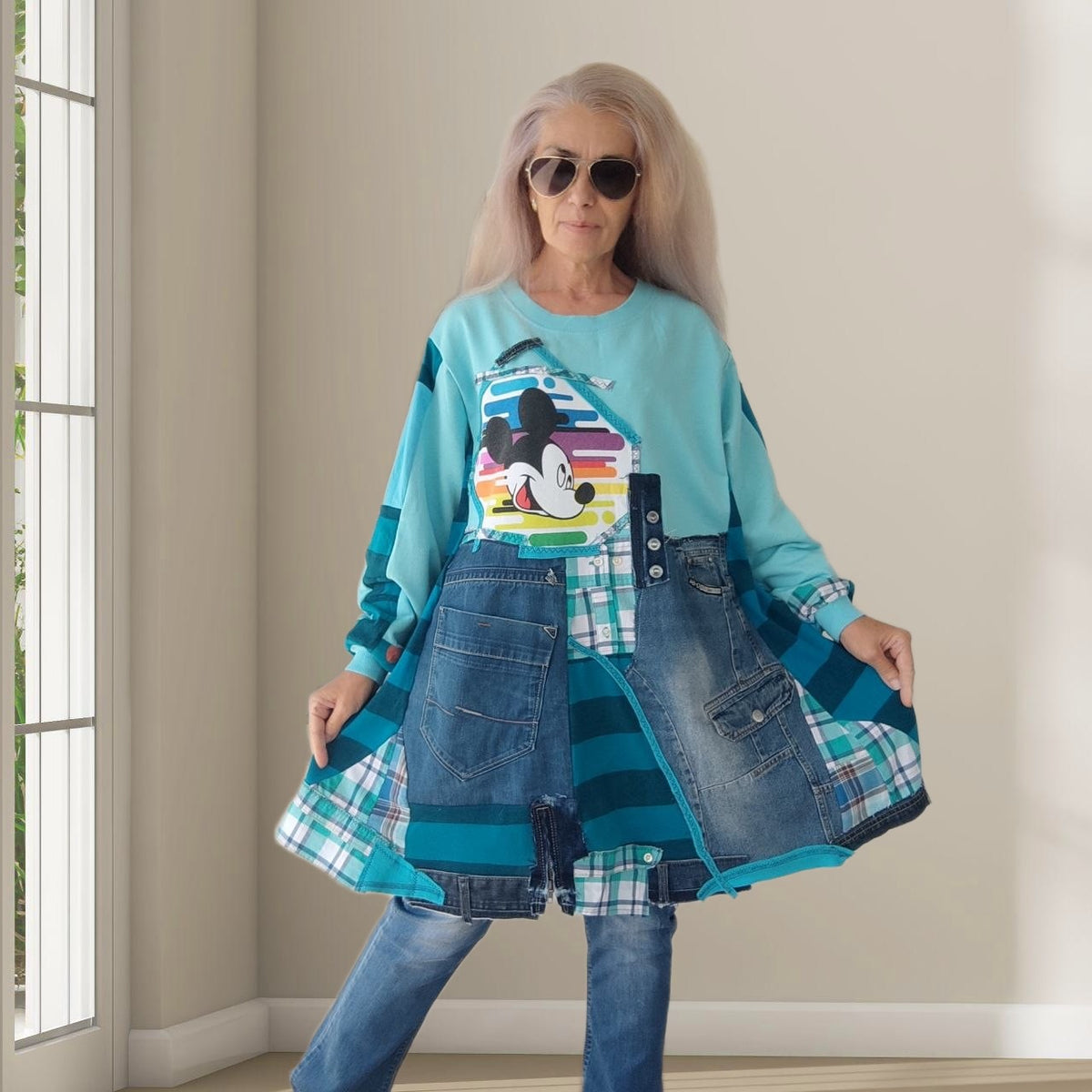 Woman modeling a handmade 3XL plus size turquoise sweatshirt dress by MARTINELI, featuring a colorful Mickey Mouse graphic, blue denim patchwork, plaid cotton panels, oversized denim pockets and a relaxed boho silhouette.