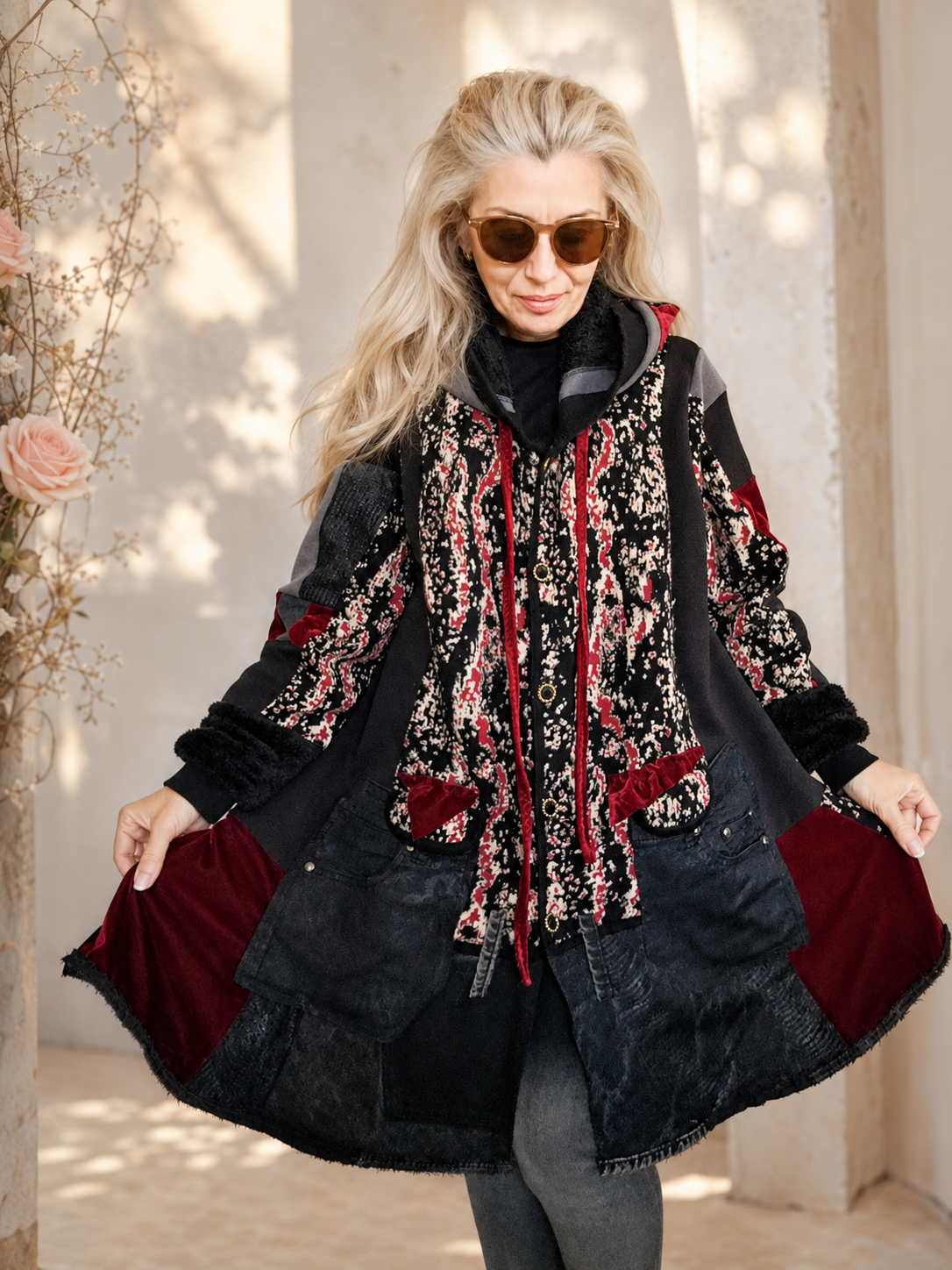 Woman modeling a handmade 3XL plus size black hooded patchwork cardigan with patterned knit fabric, dark denim panels, strawberry pink velvet pockets, furry cuffs and a flowing oversized silhouette by MARTINELI FASHION.